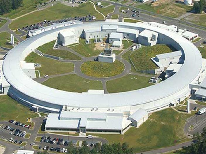 Image of a white Synchrotron seen from the air, surrounded by roads, grass, parking lots and trees