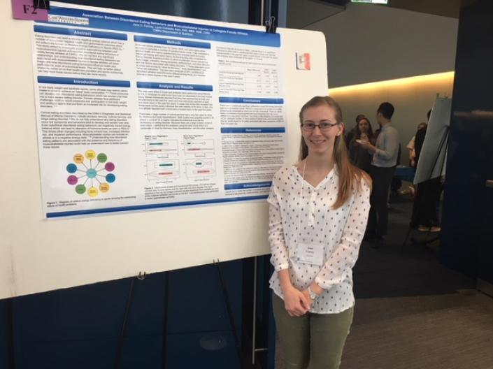 A blonde with glasses stands in front of a research poster.