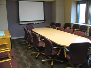 A conference room with a projector screen, table, and purple chairs