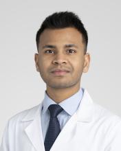 a brown skin male wearing a pale blue shirt, dark blue tie, and white coat.