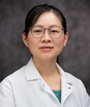 Headshot of Meinan Lyu in a white jacket and grey blurred background