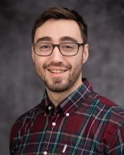 Headshot of Alex Day in a checkered collared shirt with a grey blurred background