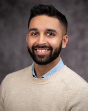 Headshot of Cian Desai in a tan sweater with a gray blurred background