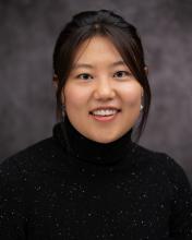 Headshot of Jean Moon in a black sweater with a grey blurred background
