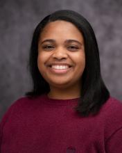 Headshot of NaShea Kendrick in a maroon top with a grey blurred background
