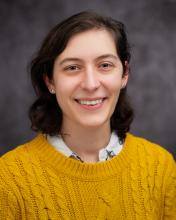Headshot of Sarah Kohrt in a yellow sweater with a grey blurred background