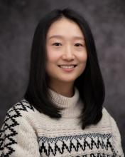 Headshot of Xu Han in a knit sweater with grey blurred background