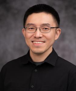 Headshot of Wei Huang in a black collared shirt with a grey blurred background