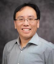 Headshot of Jack Su in a green collared button up with a grey blurred background