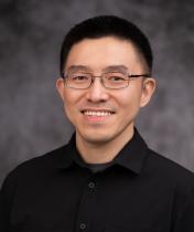 Headshot of Wei Huang in a black collared shirt with a grey blurred background