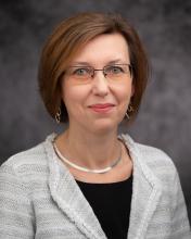 Headshot of Beata Jastrzebska in a stripped jacket and black blouse with grey blurred background