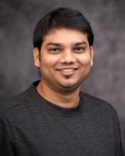 Headshot of Suraj Mandal in a grey shirt and grey blurred background