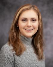 Headshot of Taylor Baker in a grey sweater with a blurred grey background