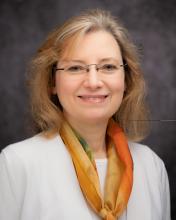 Headshot of Phoebe Stewart in a white sweater with an orange scarf and grey blurred background