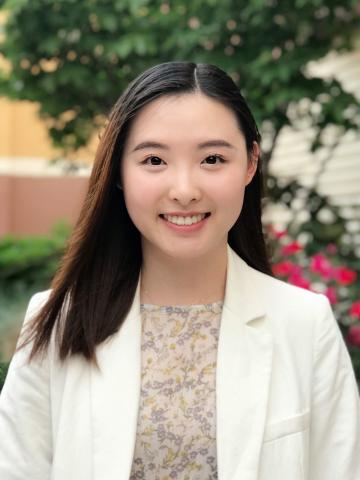 Caroline Jiang in her white coat in front of a tree