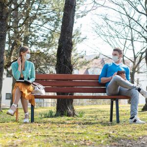 Two people sitting on a bench six feet apart