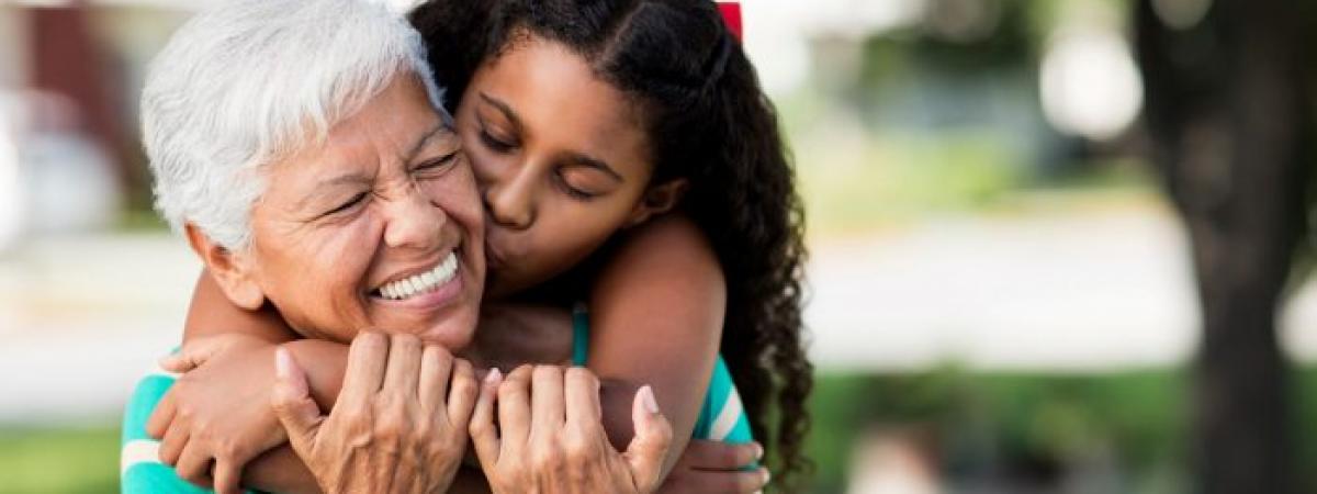 young grandaughter wrapping arms around grandmother's neck and kissing her cheek