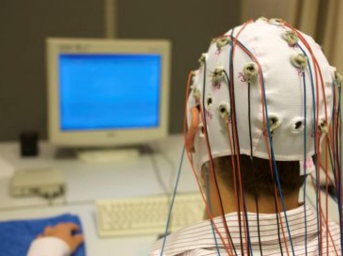 Man sitting in front of computer wearing skull cap measuring brain activity