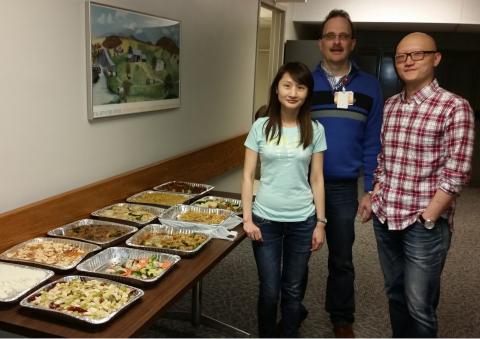 Three people standing next to a table of food smiling. 