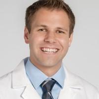 Headshot of medical student Aaron McBride in white coat and tie with grey background