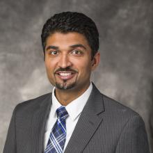 Headshot of Dr. Dan Patel in grey suit, blue striped tie, and grey background