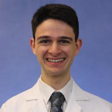 Headshot of medical student Paul Moiseyev with white coat, tie and light blue background