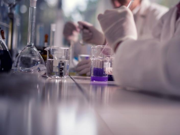 Scientists using a pipette to deposit purple liquid into beakers