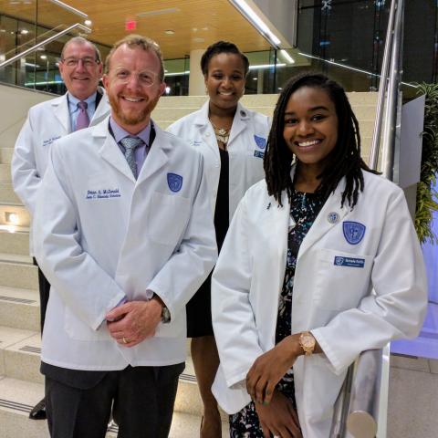 Tom McDonald (top left) and Brian McDonald (bottom left) of the Joan C. Edwards Charitable Foundation are honored by the presentation of white coats by current Edward's Scholars, Anise Bowman (top right) and Nichelle Ruffin (bottom right).