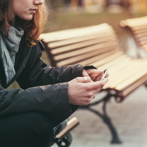 Female (face partially obstructed) sitting on bench looking at phone