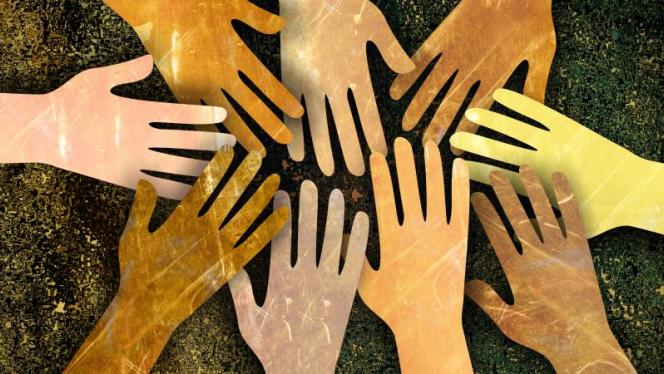 cut out hands of different shades reaching out to each other under a brown wood background