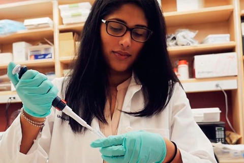 Female PREP scholar in white coat working with a pipette at a lab bench