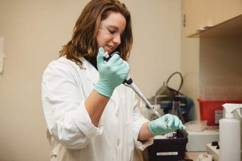 Young woman researcher in a white lab coat uses a pipette