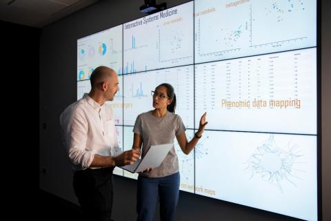 Two people reviewing data on 9 wall screens