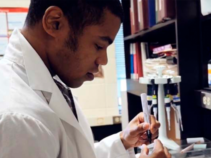 CWRU PREP student works in a white lab coat conducting research at black lab bench