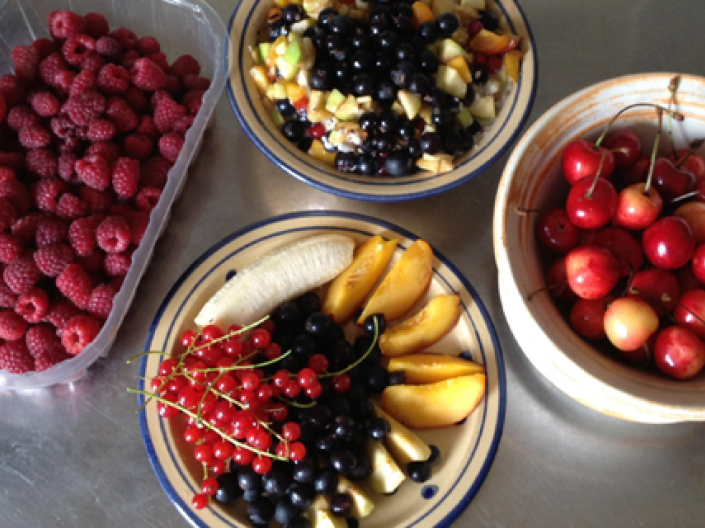 A selection of health foods consisting of a carton of raspberries, bowl of cherries, bowl of assorted fruits, and a bowl of fruit salad topped with blueberries 