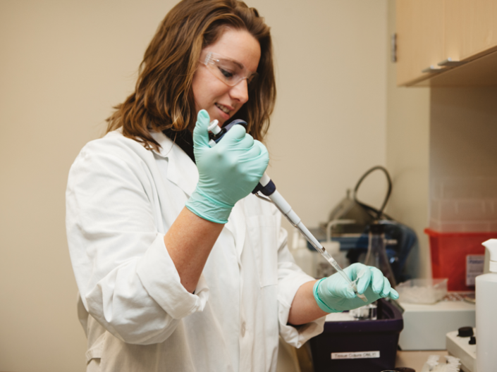 Young woman researcher in a white lab coat uses a pipette