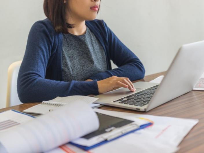 A woman in blue typing on a laptop