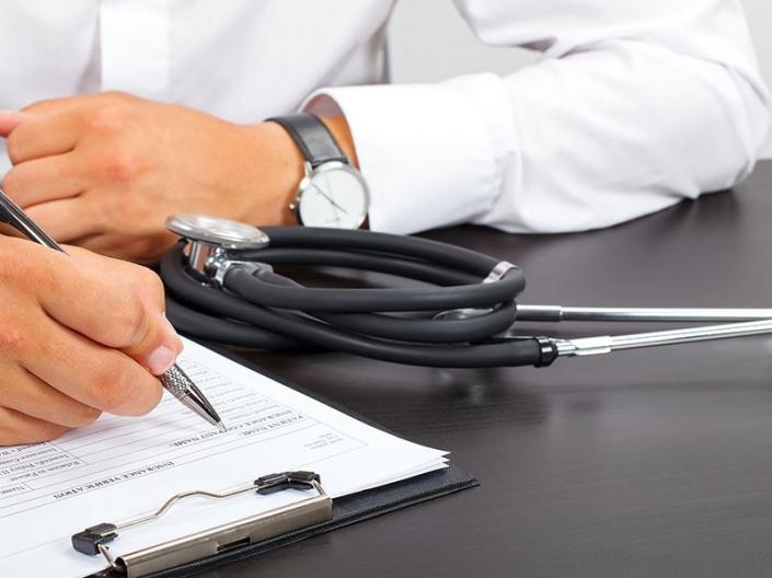 A doctor filling out paperwork with a stethoscope beside them