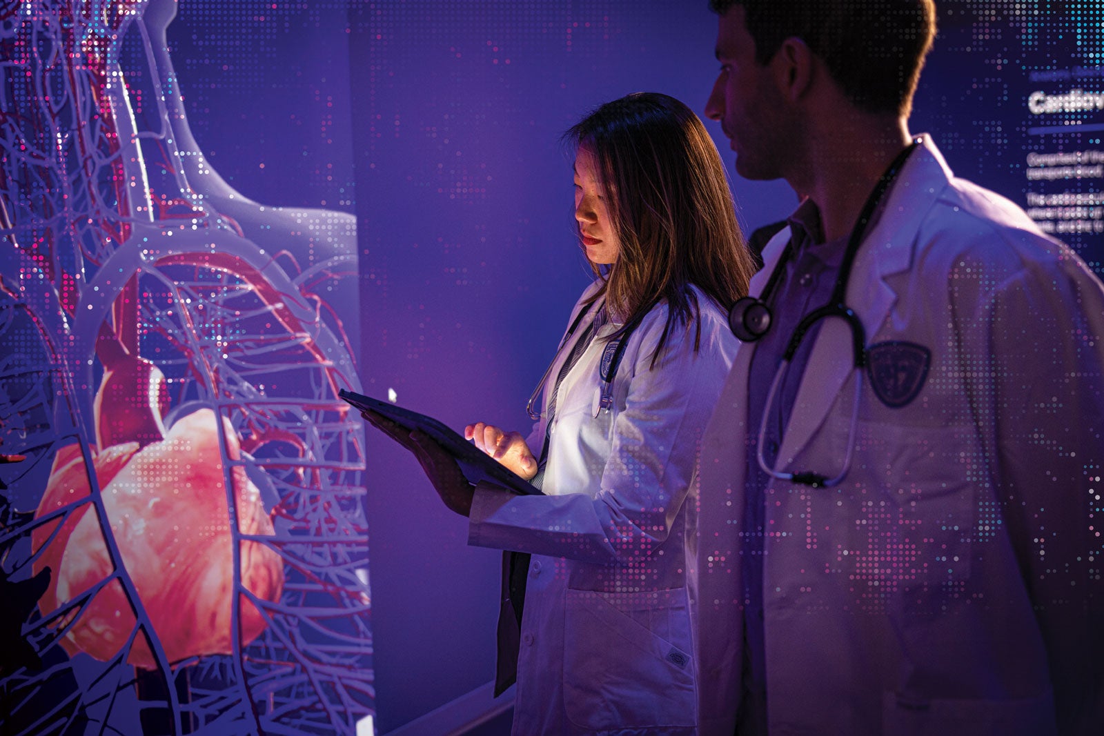 Two Case Western Reserve University medical students stand in a dark room looking at a hologram of a body on a wall