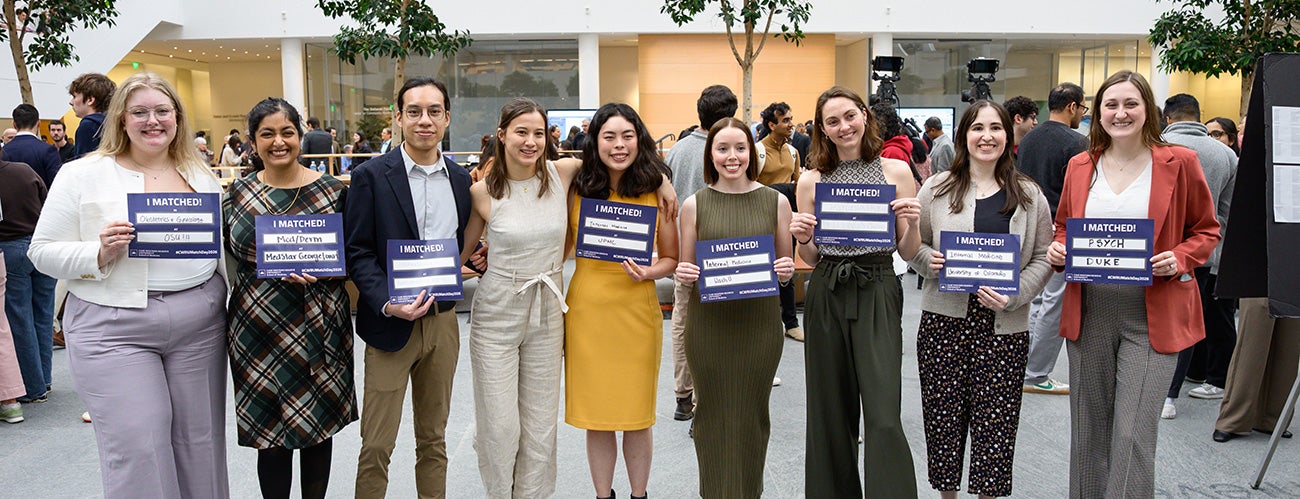 Med students stand together and smile for a photo with their Match Day papers.