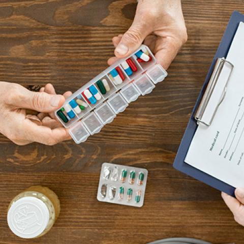 stock image of hands holding pill box filled with medications and someone with white coat holdling a clipboard