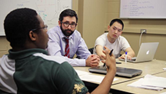 Three men of various backgrounds sit in a conference room and discuss.