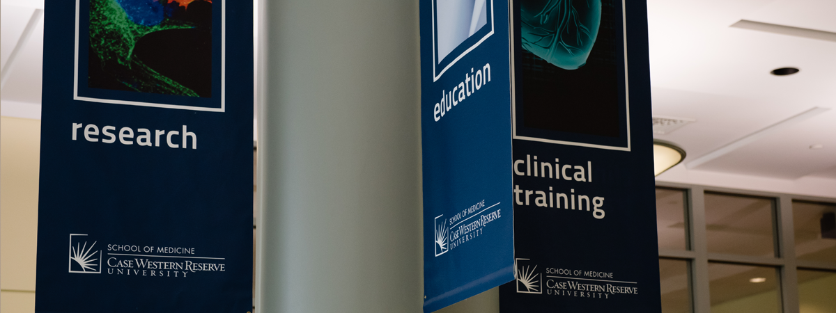 Three hanging blue banners each with the School of Medicine logo at the bottom and displaying the word "Research," "Education," or "Clinical Training."