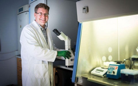 Researcher Tilton Chip standing in front of microscope in lab smiling towards camera