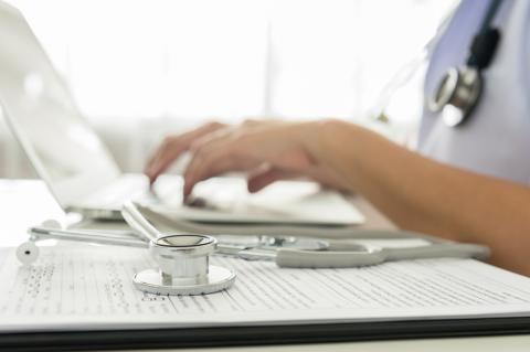 Close up of hands typing on a computer next to a stethoscope 