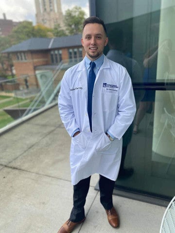 Blake Harvey wearing whtie coat standing outside a door