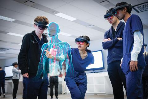 A group of Case Western Reserve University medical students wearing headsets look at a holographic body floating in the middle of the room