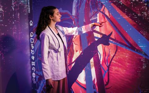 A Case Western Reserve University medical student points at part of the body on a holographic image on a wall
