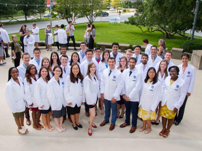A group of 30 medical students stand together in their new white coats at the CWRU Medical School White Coat Ceremony