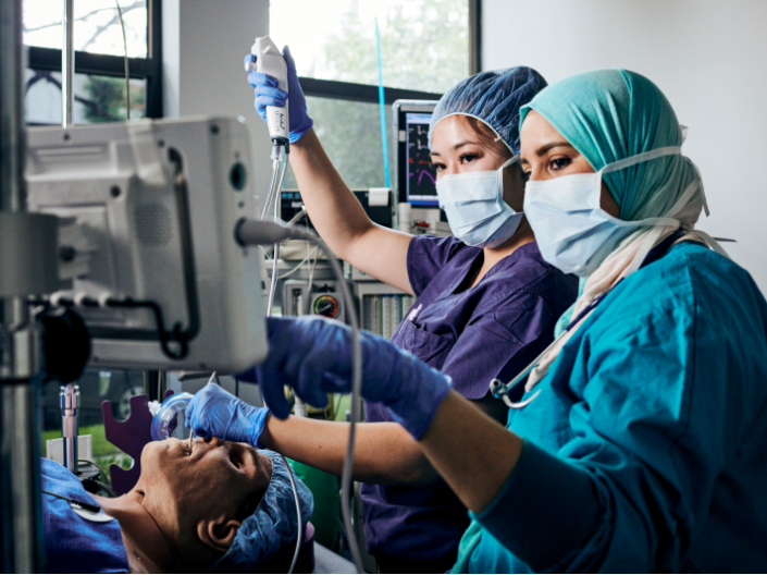 Two students in full scrubs work with a dummy to practice anesthesiology